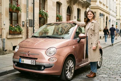 Fiat 500 rose gold garée dans une rue pavée européenne avec une jeune femme appuyée sur la portière