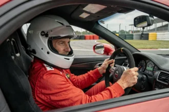 Pilote en combinaison rouge au volant d'une voiture de sport sur circuit lors d'un stage de pilotage