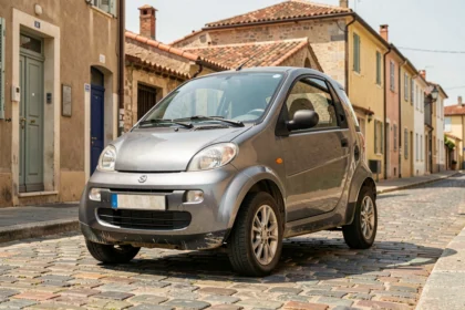 Voiture sans permis d'occasion de couleur gris métallisé garée dans une rue pavée de Perpignan avec des bâtiments aux toits en tuiles