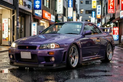 Nissan Skyline GT-R R34 en finition violet métallisé garé dans une rue urbaine japonaise sous la pluie, vue 3/4 avant surélevée mettant en valeur la carrosserie large et les feux arrière ronds emblématiques